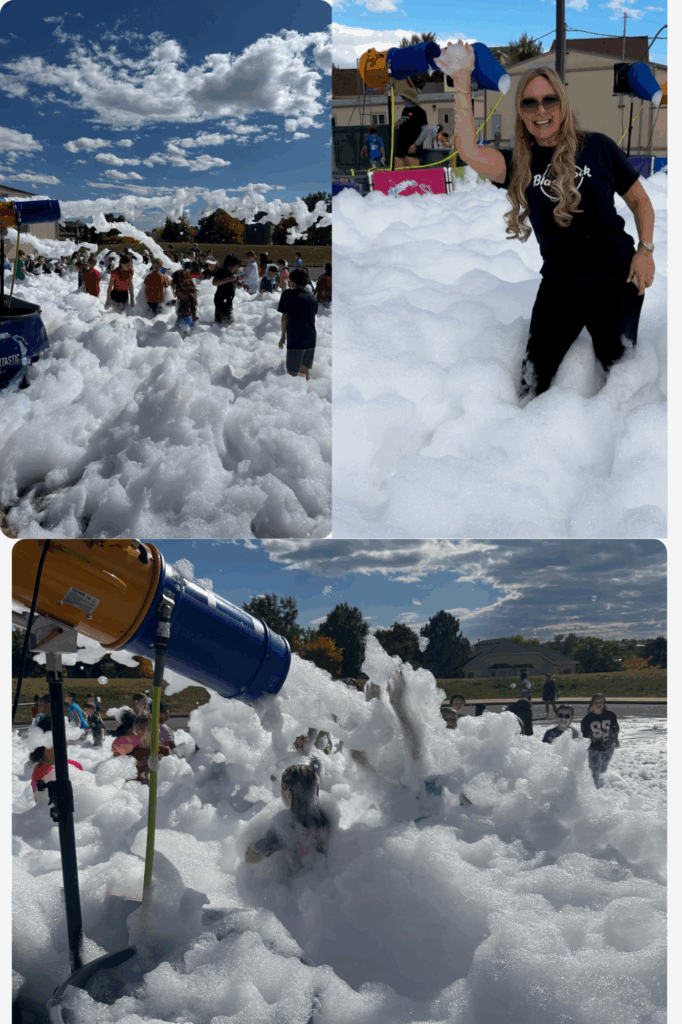 Children play in a large foam area with a foam machine, under a blue sky with scattered clouds.