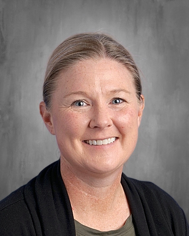 Smiling woman with light brown hair, wearing a black cardigan, against a gray background.