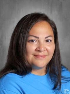 A woman with long dark hair smiles, wearing a blue shirt, set against a neutral background.