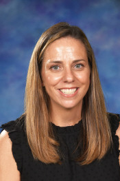 Smiling woman with long, straight hair, wearing a black top, against a blue background.