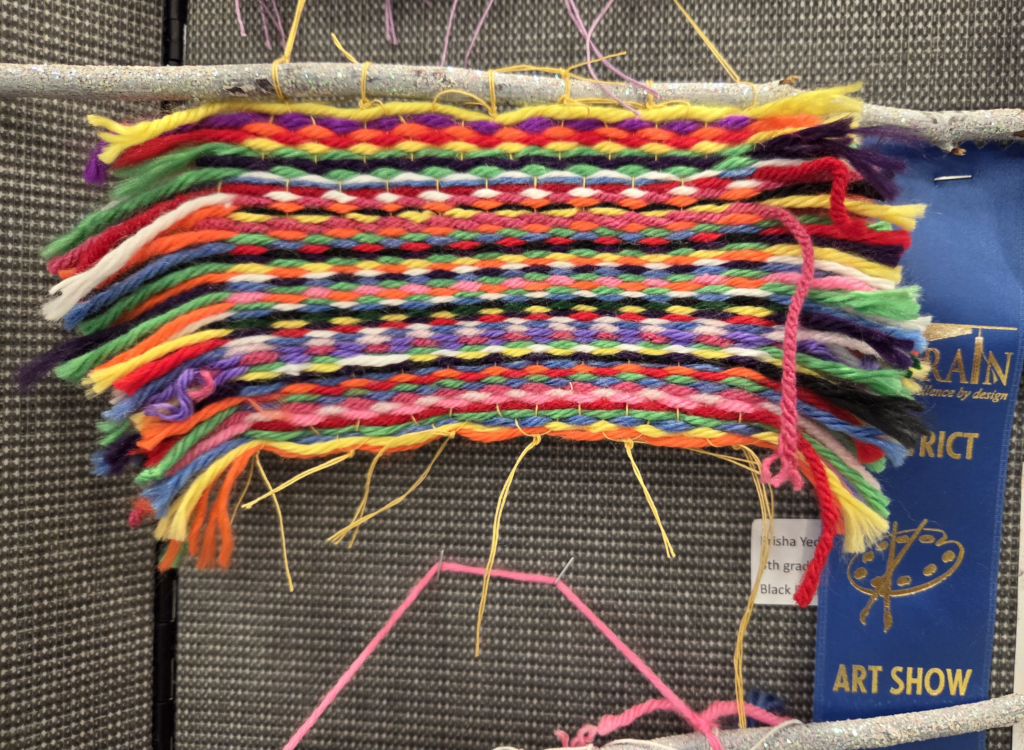 Colorful woven yarn samples displayed at an art show, showcasing various patterns and textures.