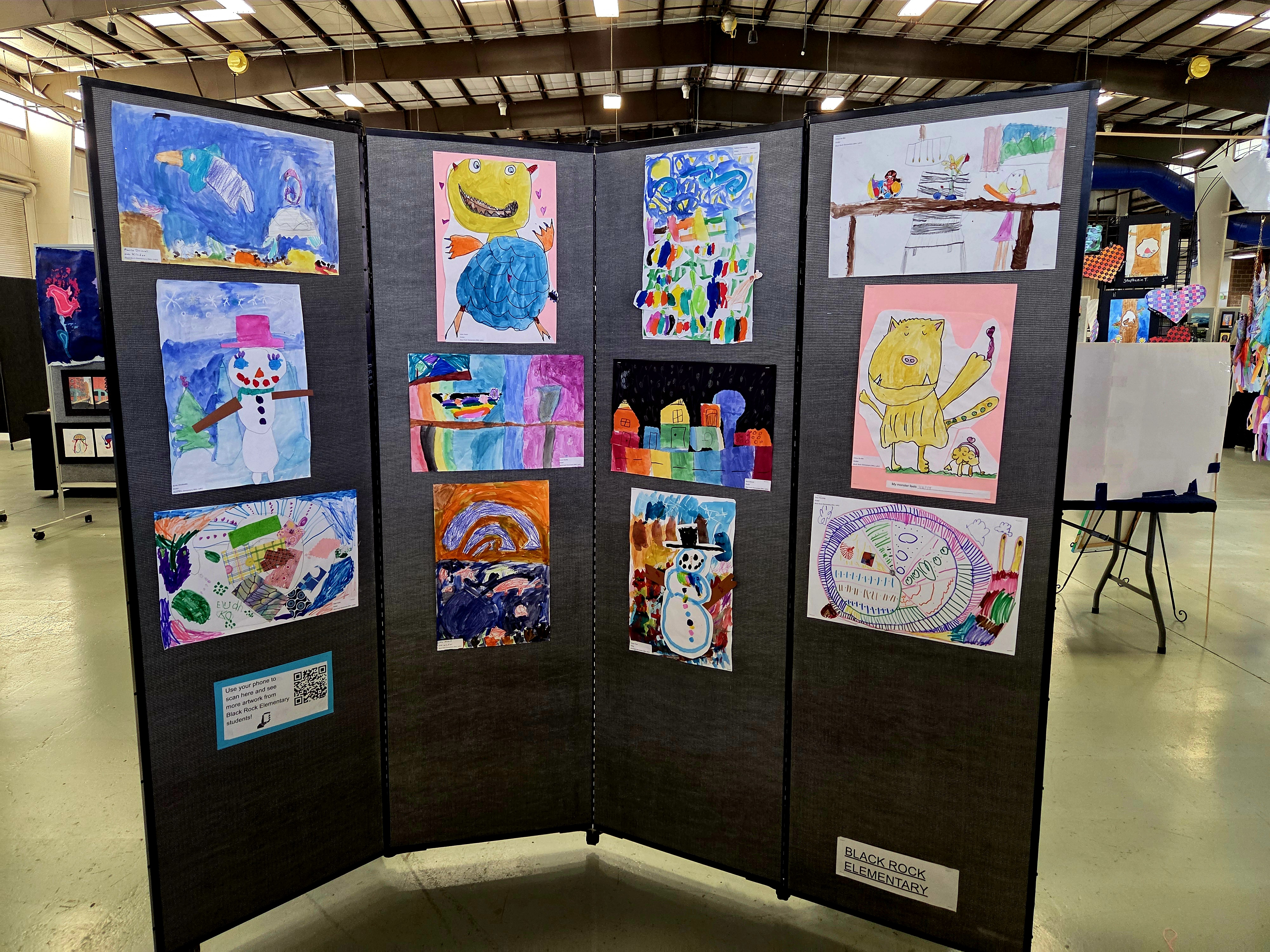 Art display featuring colorful children's drawings on a tri-fold board, showcasing various themes and subjects.