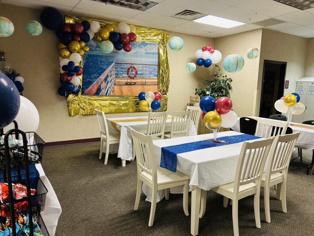 Decorated party room with tables, colorful balloons, and a maritime-themed mural featuring a dock and lifebuoy.