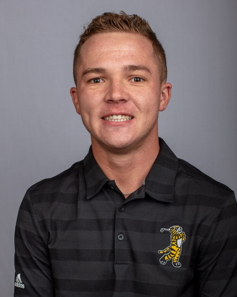 A young man smiles in a black striped polo shirt featuring a golfing tiger logo, with a gray background.